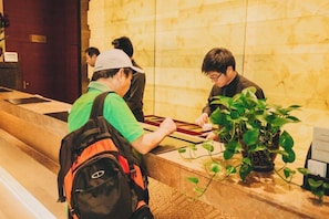 A reception area with a reception desk, a potted plant, and a person seated at the desk. - Yucheng Hotel (Suzhou)