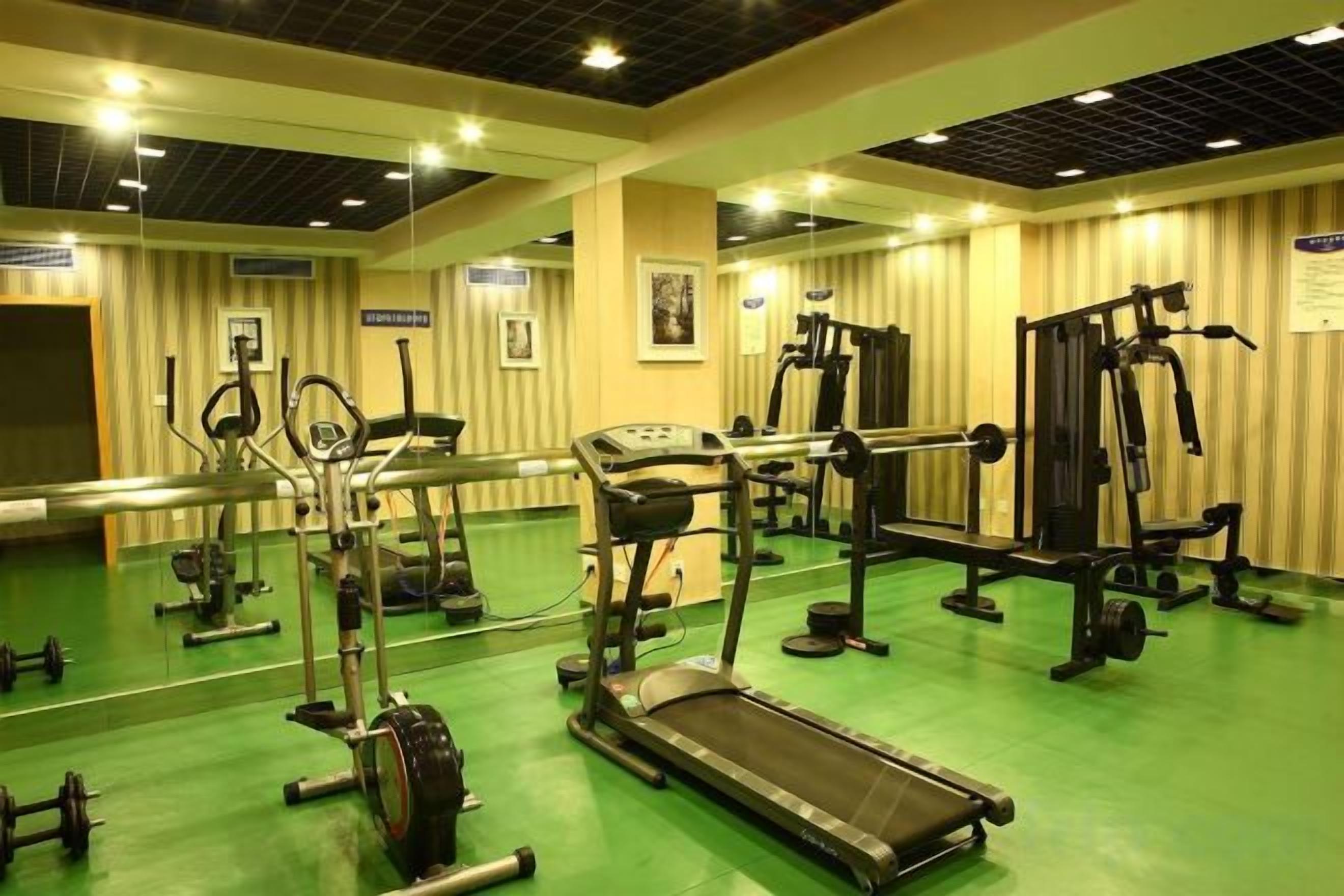 A gym with exercise equipment, a mirrored wall, and a green floor.