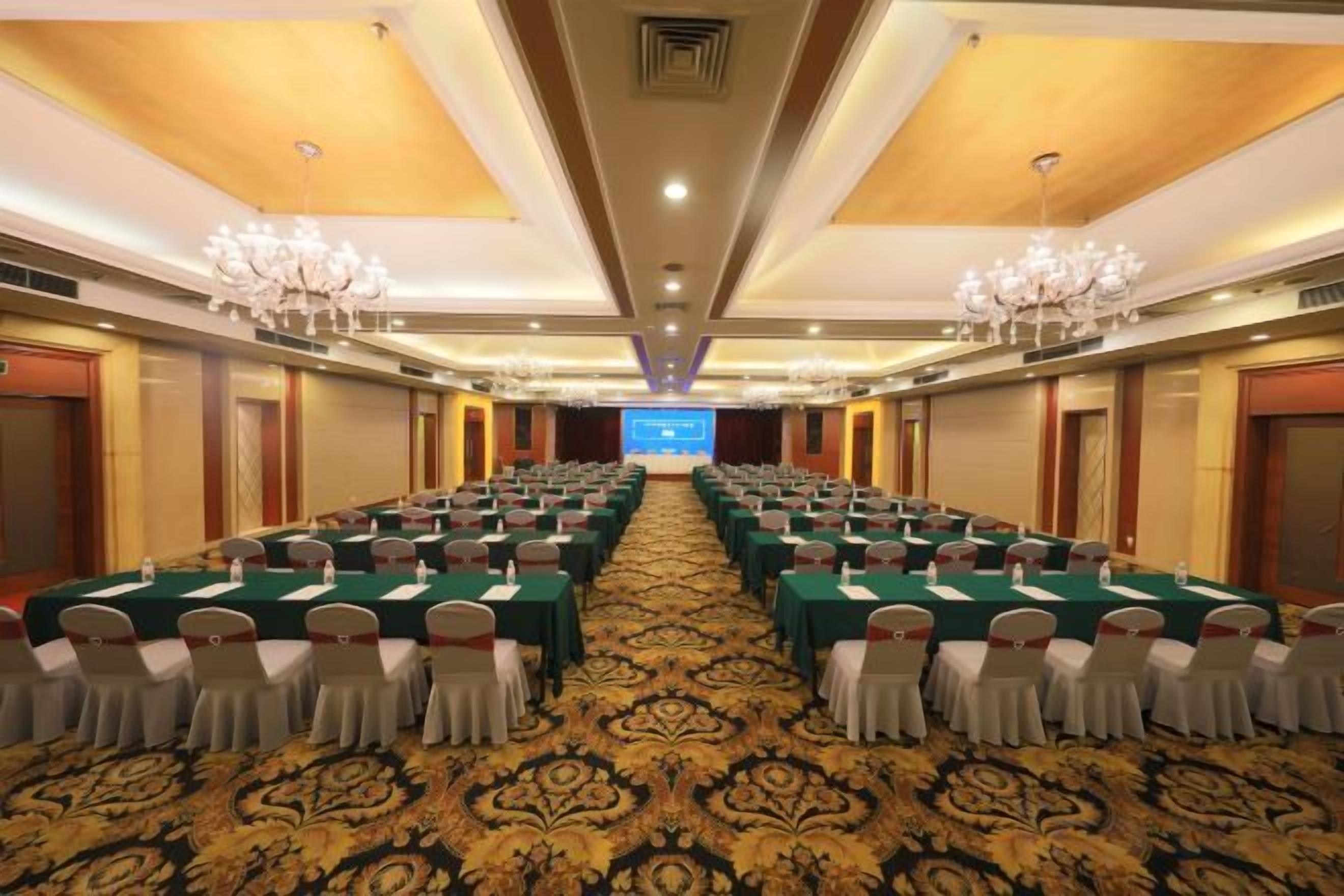 A conference room with rows of tables and chairs, a carpeted floor, and chandeliers.