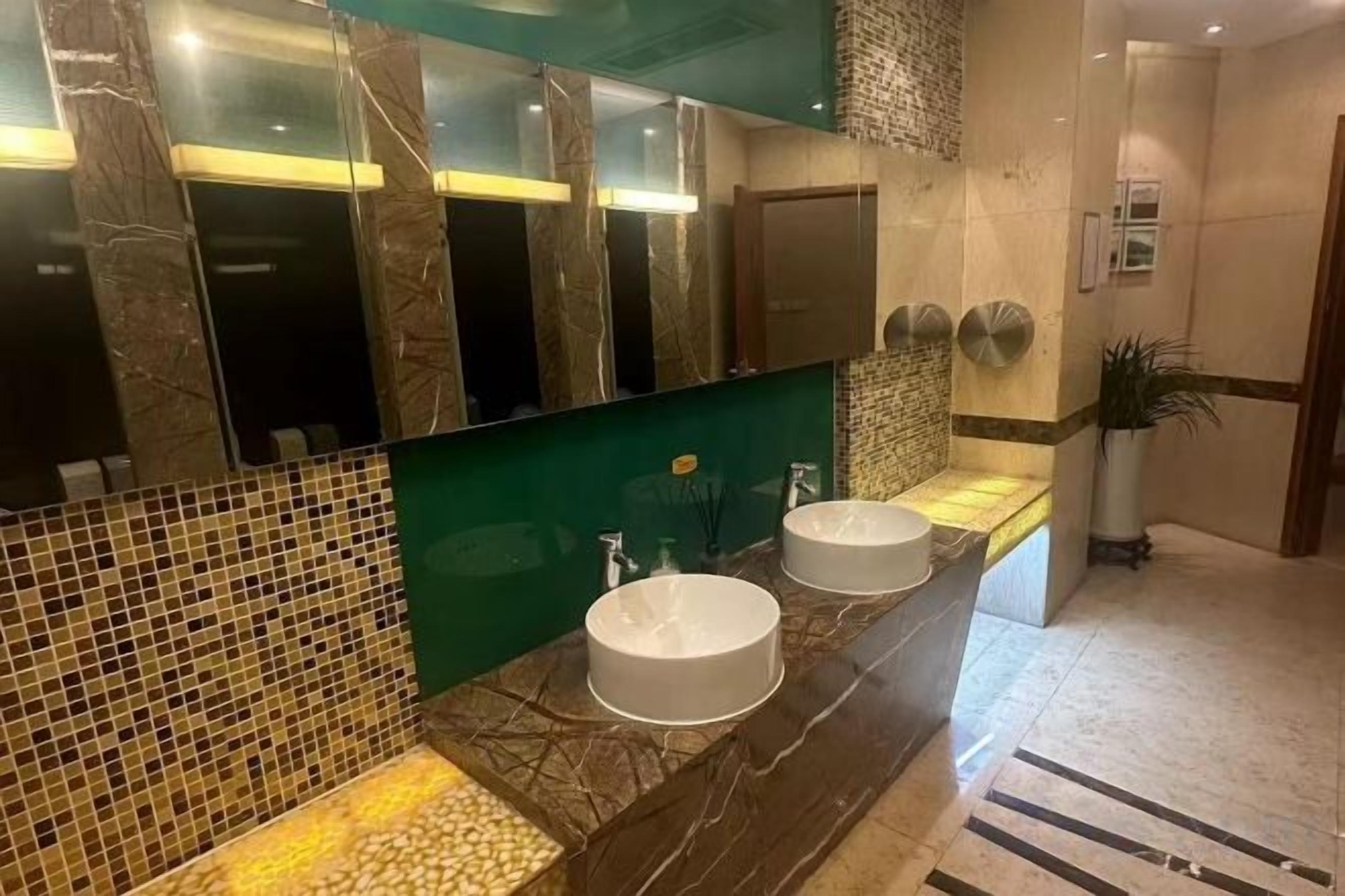 Casa de banho com duas pias, um espelho grande e uma parede verde decorativa.