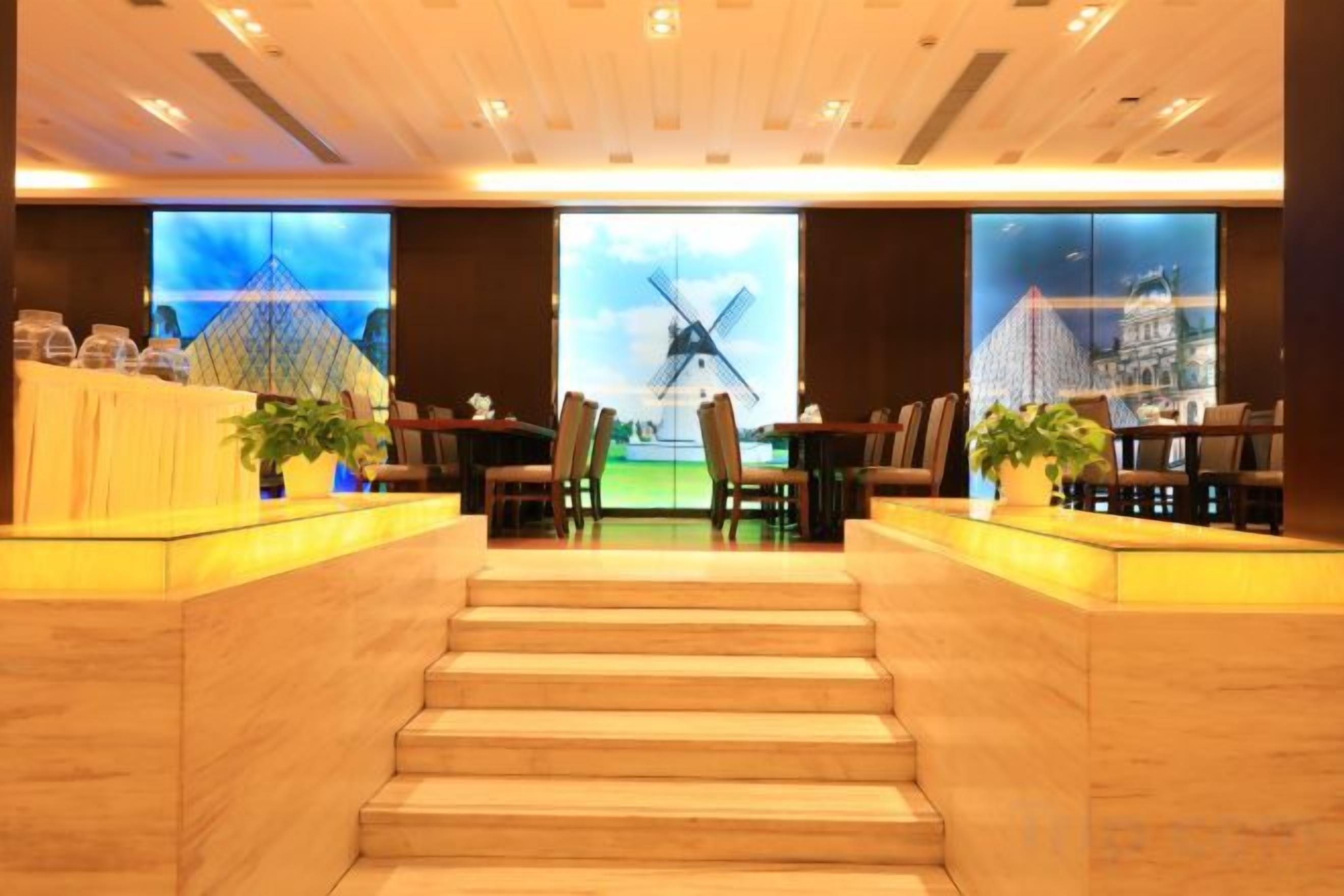 A hotel lobby with a staircase leading to the upper floor, a reception desk, and a large window with a view of a windmill.