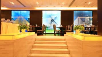 A hotel lobby with a staircase leading to the upper floor, a reception desk, and a large window with a view of a windmill.
