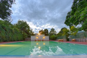 A swimming pool with a stone wall and seating area, surrounded by trees and a cloudy sky. - Swat Serena Hotel (Swat)