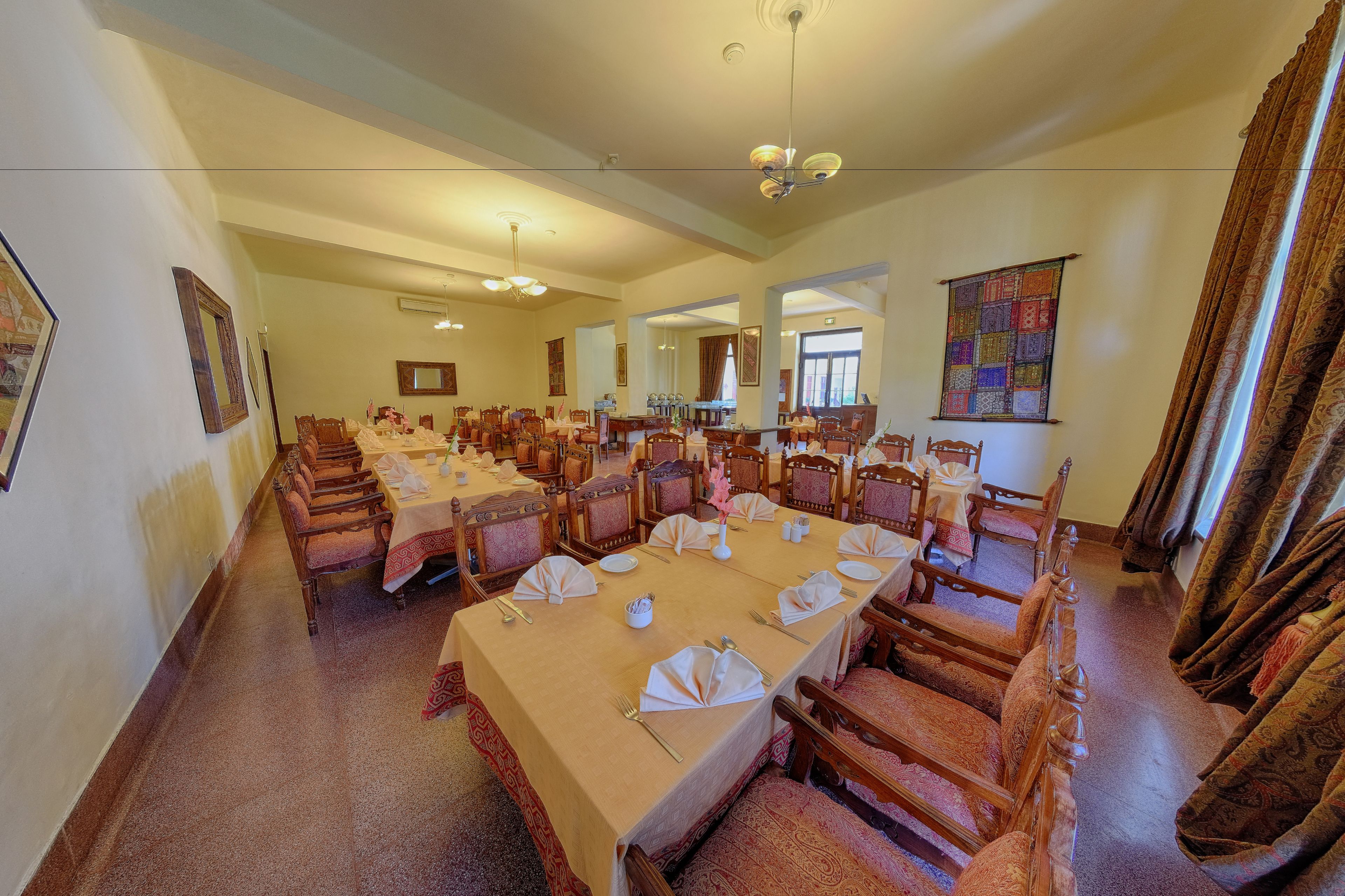 A large dining hall with long tables set for a meal, wooden chairs, and a chandelier.