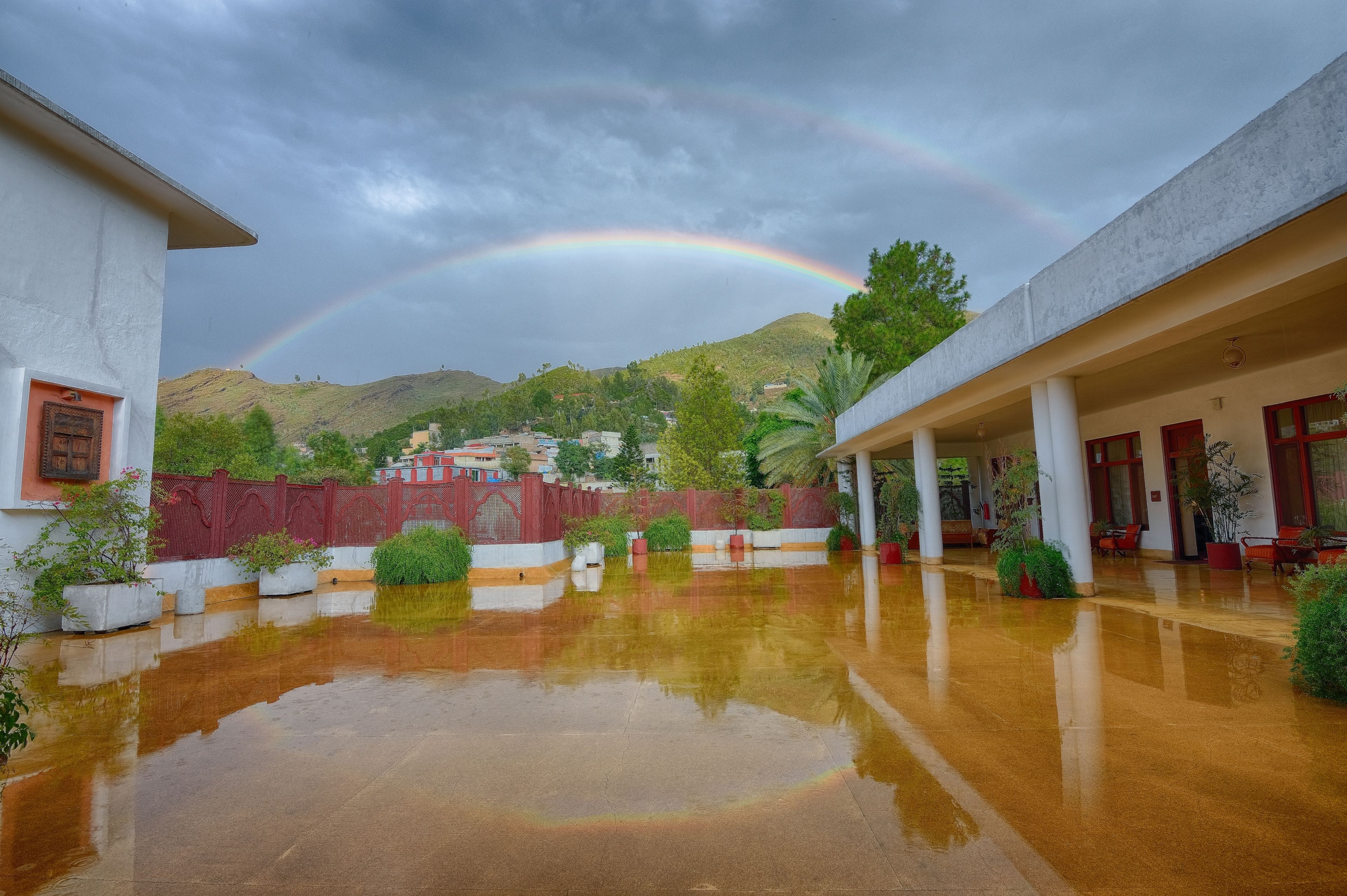 A covered outdoor area with a reflective wet floor, a red fence, and a mountain in the background.