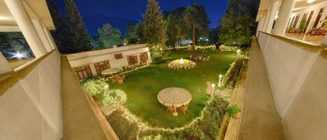 Un jardín exterior bien iluminado con un espacio de estar circular, rodeado de follaje y árboles.