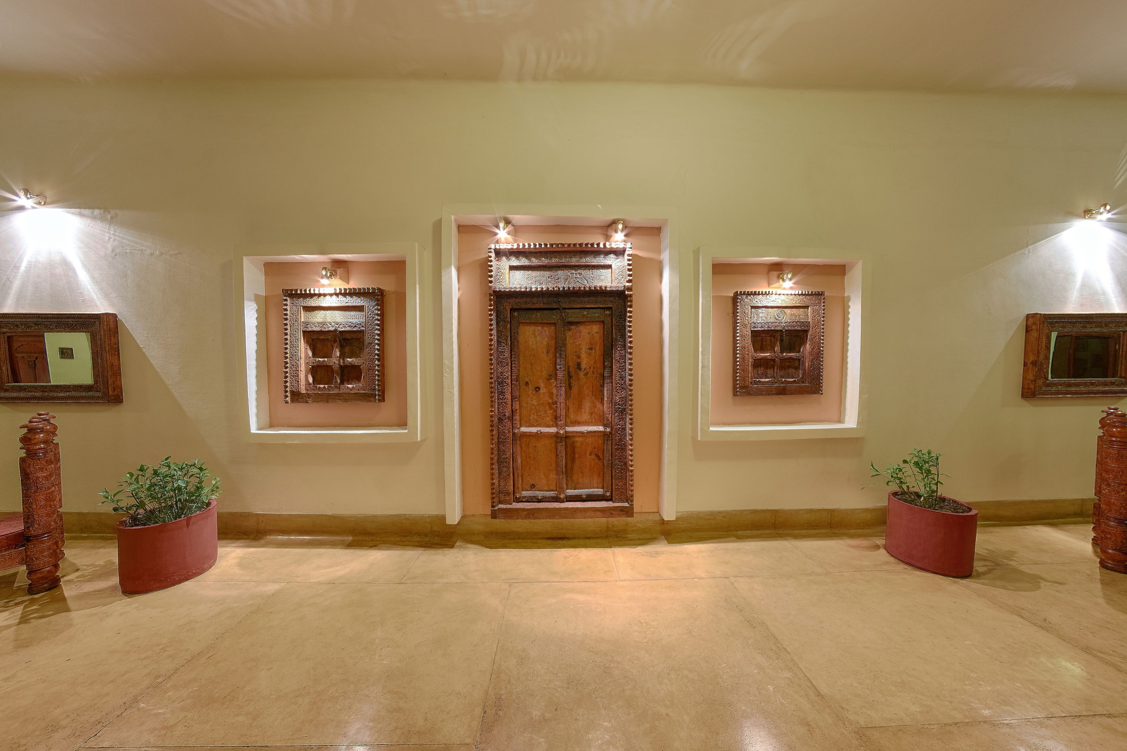 A hallway with a central wooden door flanked by two framed mirrors and potted plants.