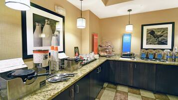 A hotel kitchen with granite countertops, stainless steel appliances, and a variety of food items and utensils.
