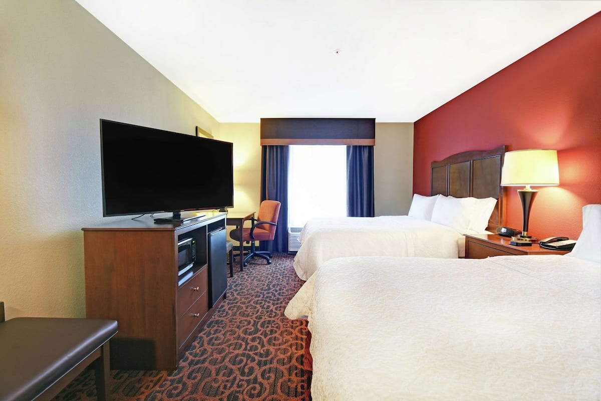 A hotel room with two beds, a TV, a desk, a chair, and a lamp.