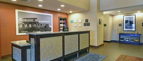 A hotel reception area with a counter, framed pictures on the wall, and a welcome mat.
