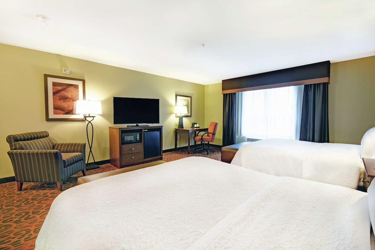 A hotel room with two beds, a desk with a television, a chair, and a lamp.