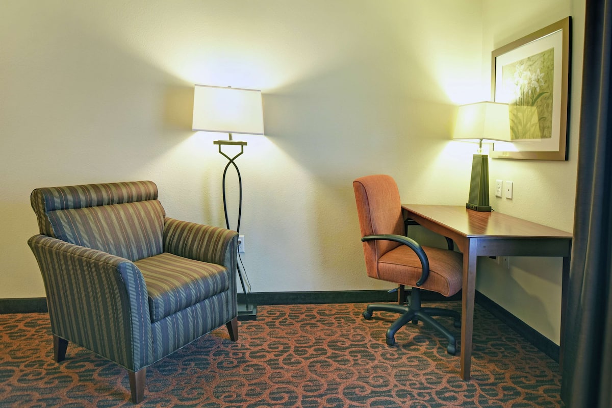 A hotel room with a striped armchair, an office chair, a desk, and two floor lamps.
