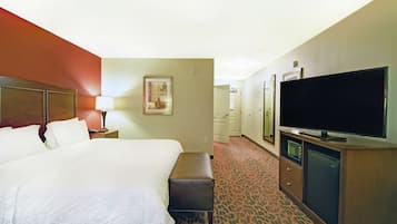 A hotel room with a large bed, a flat-screen TV, a desk with a lamp, a microwave, and a refrigerator.
