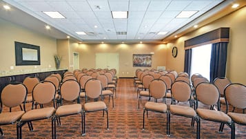 A conference room with rows of chairs, a carpeted floor, a clock, and a large window with curtains.