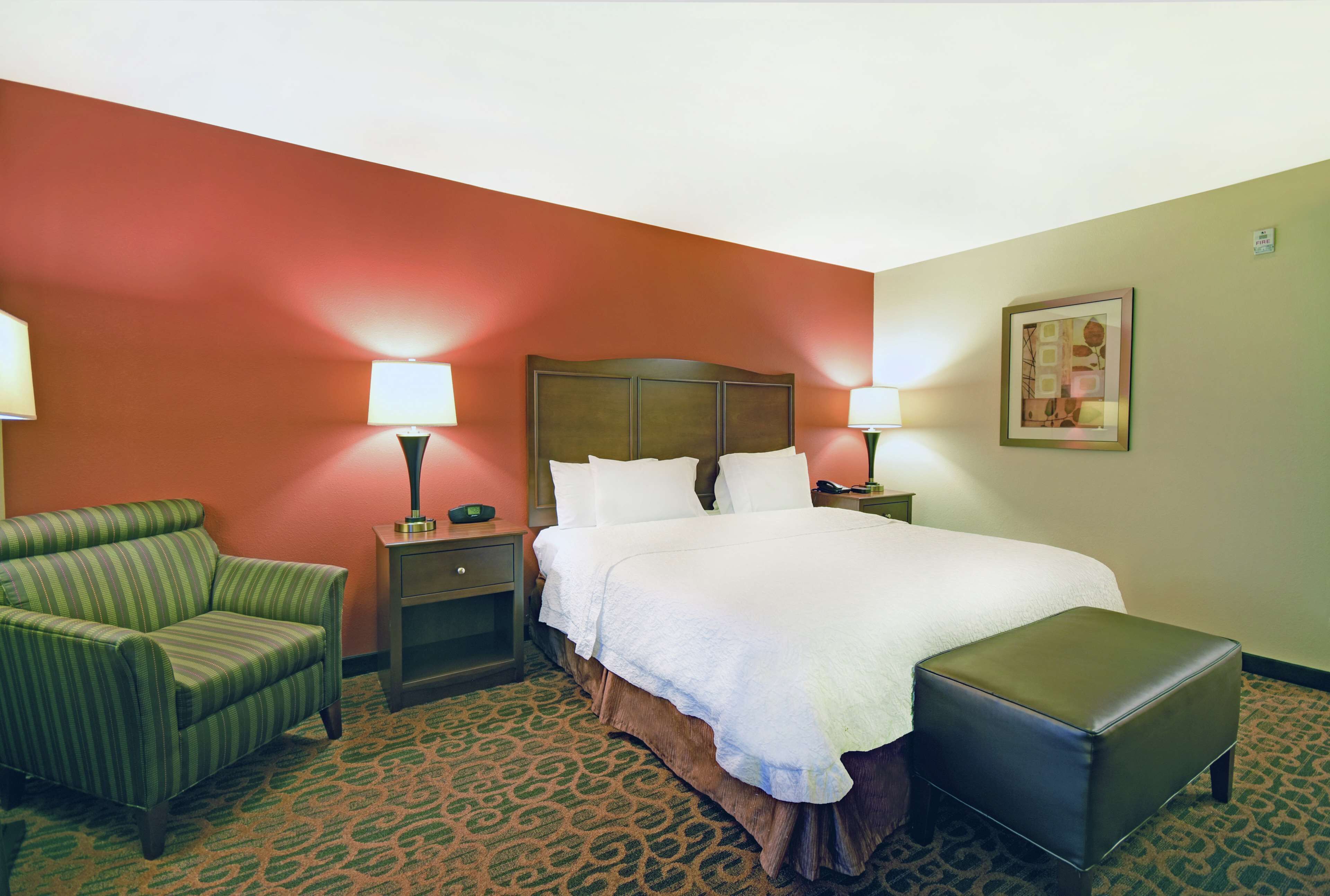 Une chambre d’hôtel avec un lit, une chaise, une table de chevet et une lampe.