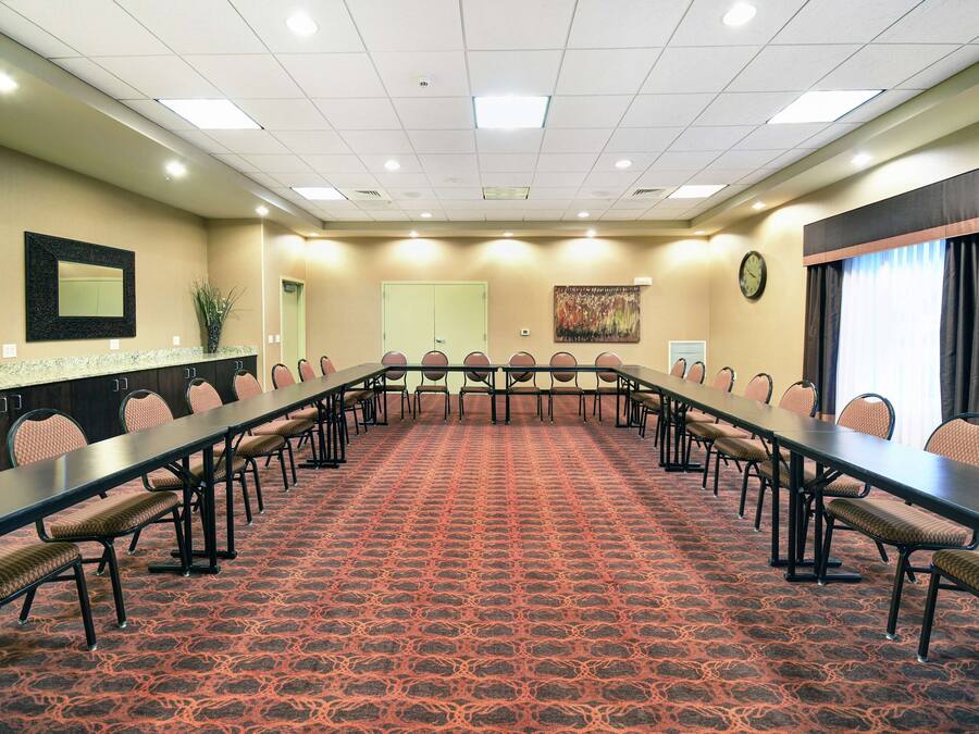 A conference room with a long table, chairs, carpeted floor, and a clock on the wall.
