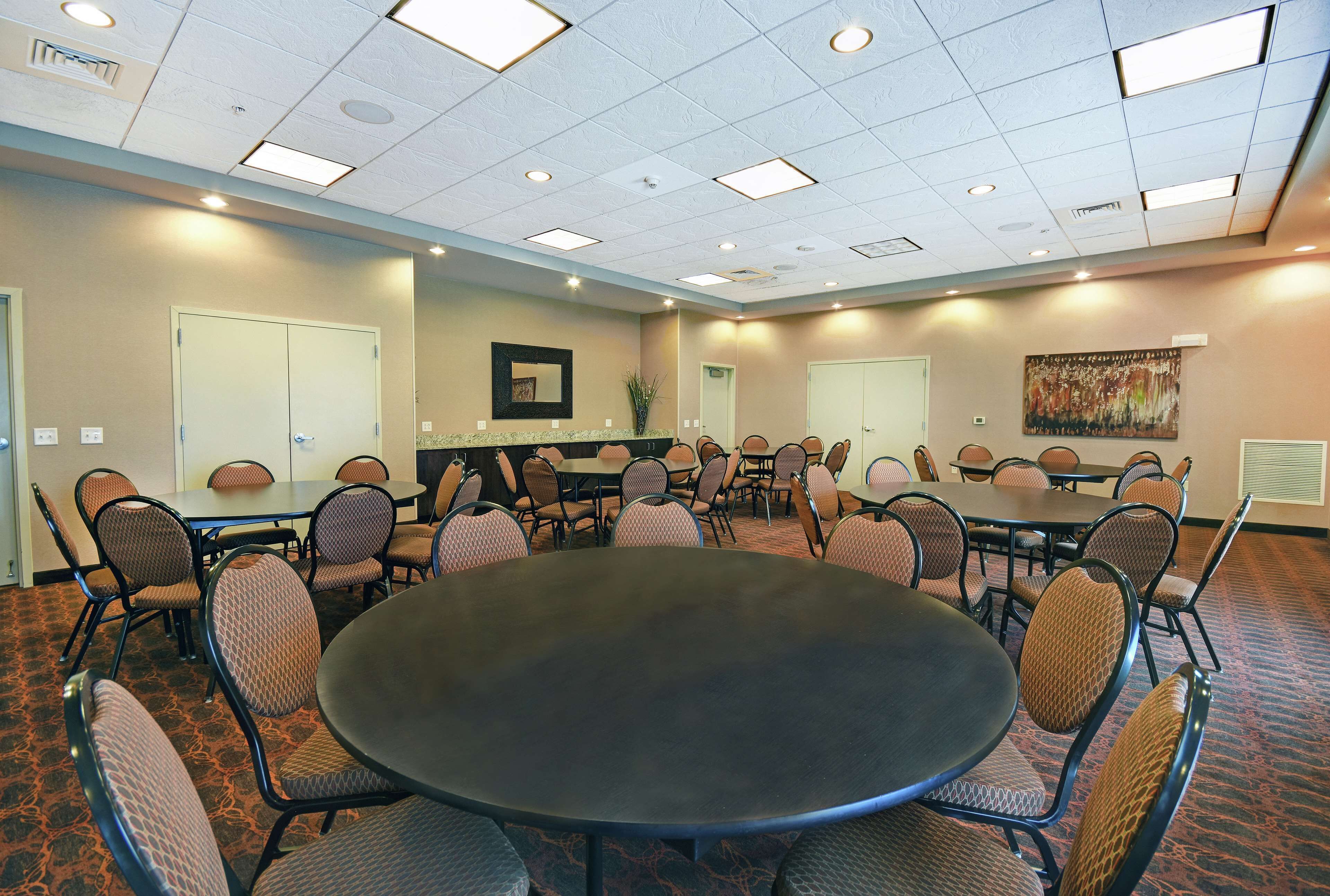 A conference room with a large round table surrounded by chairs, a whiteboard, and a painting on the wall.