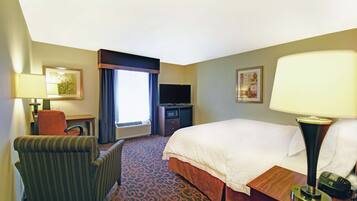 A hotel room with a bed, a desk, a chair, a television, and a lamp.