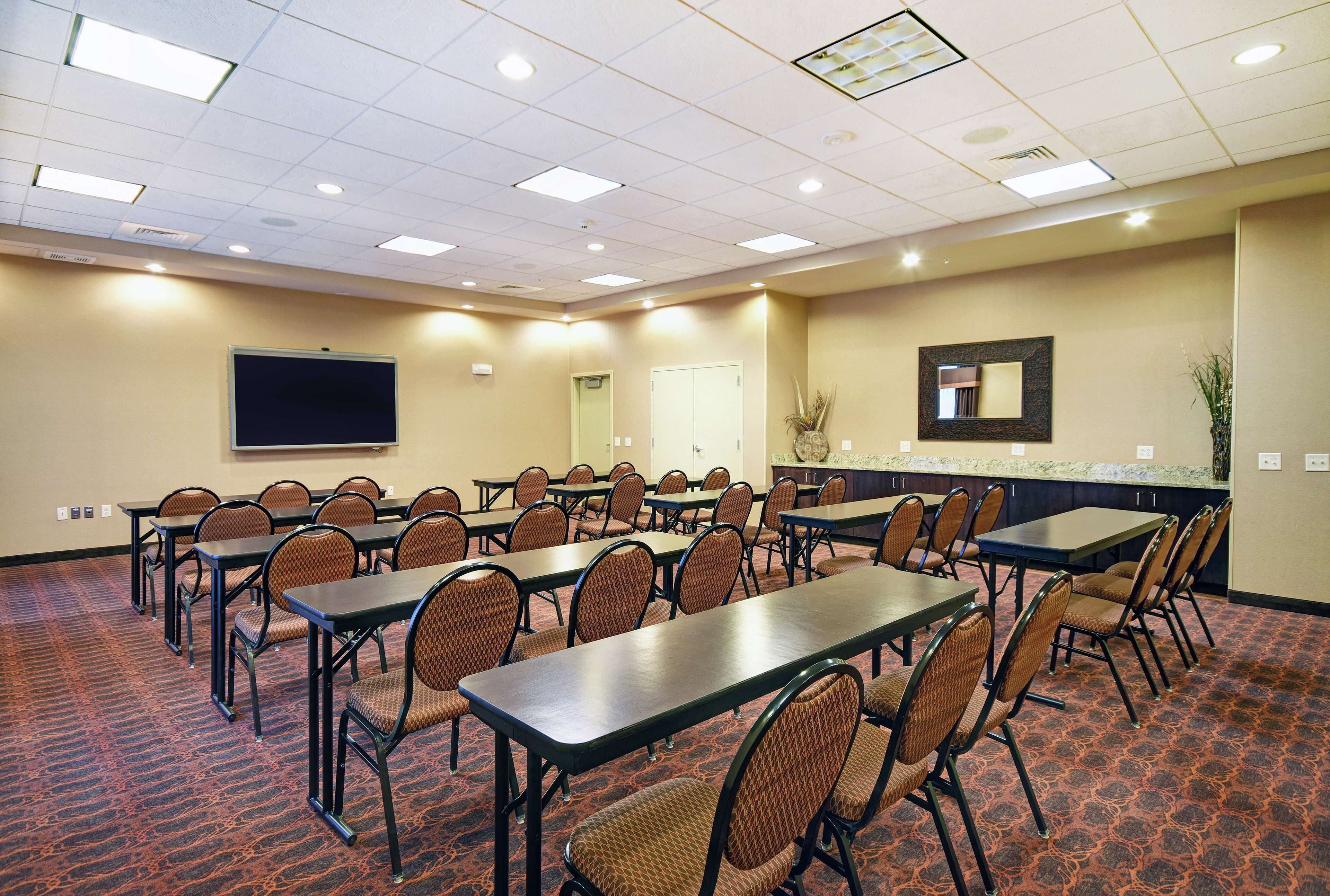 Une salle de conférence équipée de plusieurs tables et chaises, d’un grand écran et d’un comptoir avec un miroir.