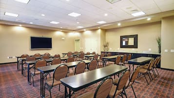 Une salle de conférence équipée de plusieurs tables et chaises, d’un grand écran et d’un comptoir avec un miroir.