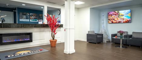 A hotel lobby with a reception desk, a fireplace, a large window, and a seating area.