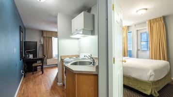 A compact hotel room with a kitchenette, a bed, a desk, and a television.