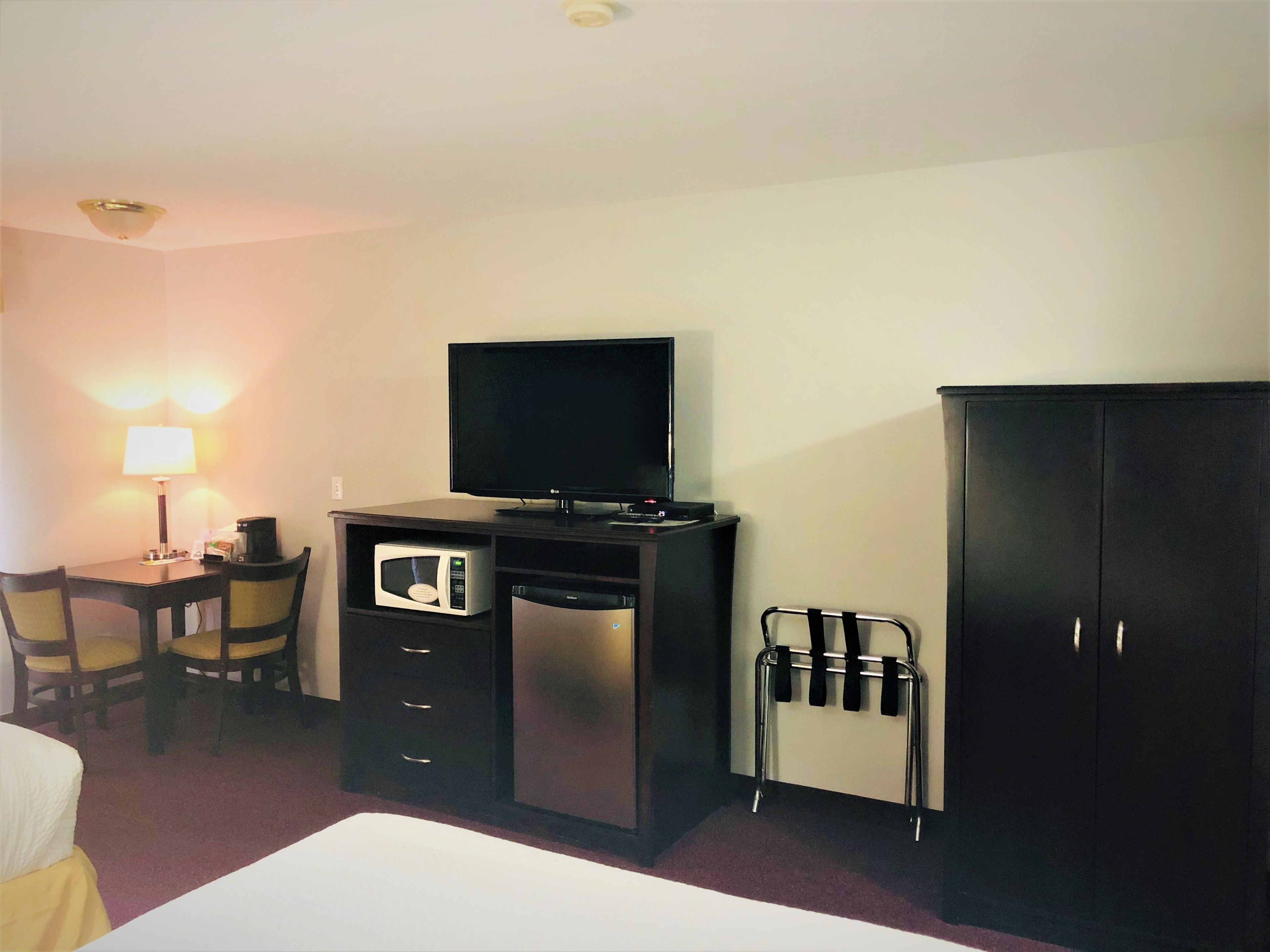 A hotel room with a bed, a desk with a lamp, a microwave, a TV, and a wardrobe.