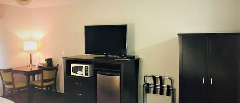 A hotel room with a bed, a desk with a lamp, a microwave, a TV, and a wardrobe.