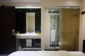 Ein Hotelzimmer mit einem großen Bett, einem Badezimmer mit einem modernen Waschbecken und Spiegel sowie einer Dusche mit Glastür.