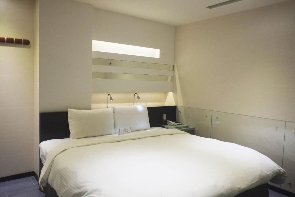 A hotel room with a large bed, a bedside table, a lamp, and a wardrobe.