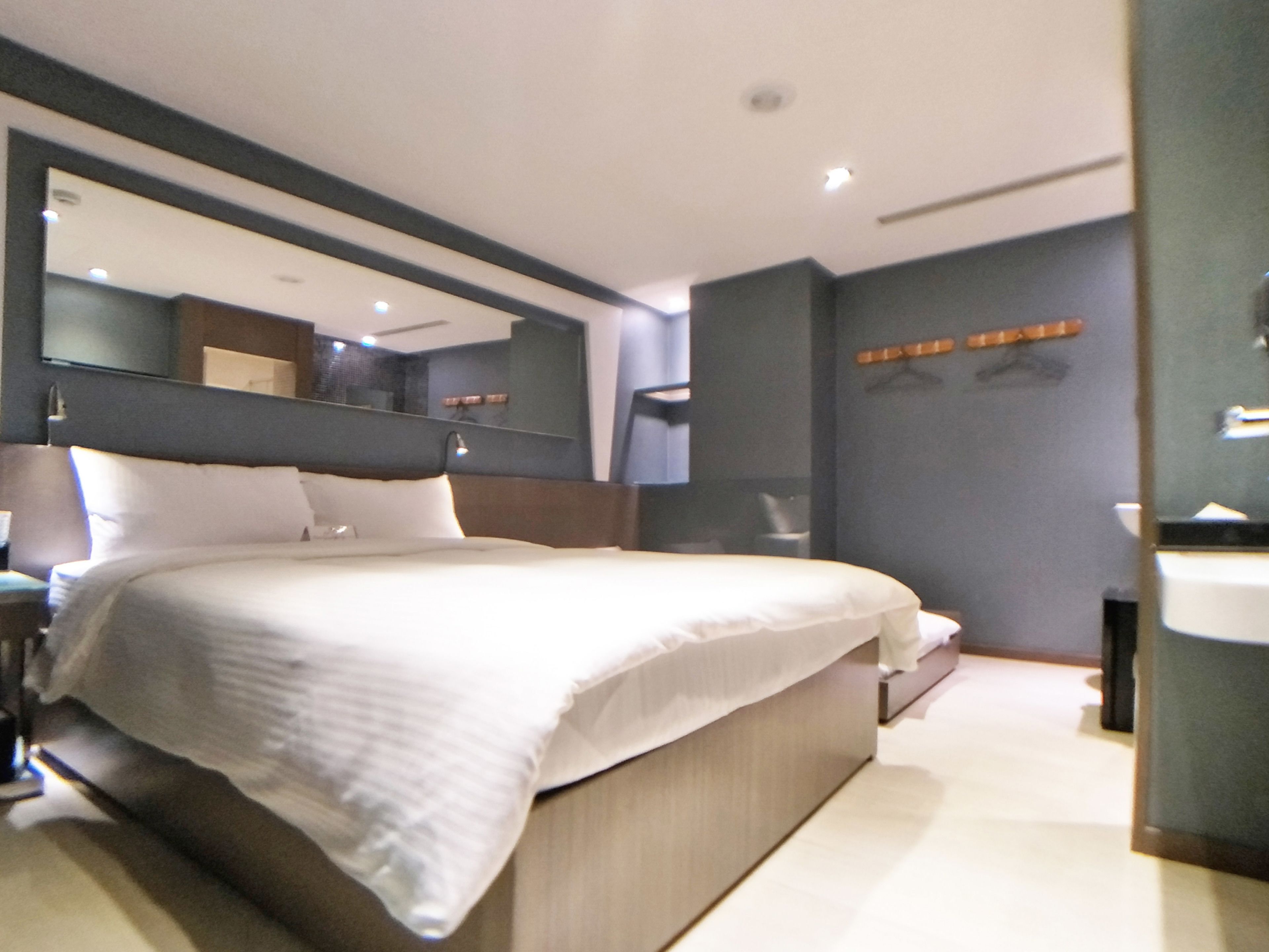 A modern hotel room with a large bed, a bedside table, a mirror, and a built-in bench.