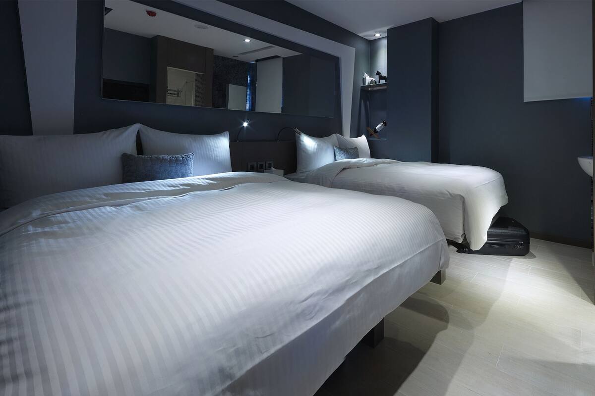 Moderni hotellihuone, jossa on kaksi sänkyä, suuri peili ja pieni kylpyhuone.