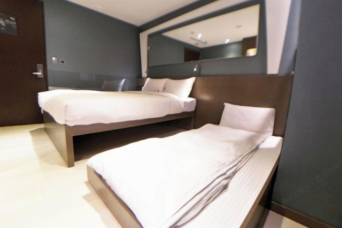 Une chambre d’hôtel avec deux lits simples, un grand miroir et une tête de lit en bois.