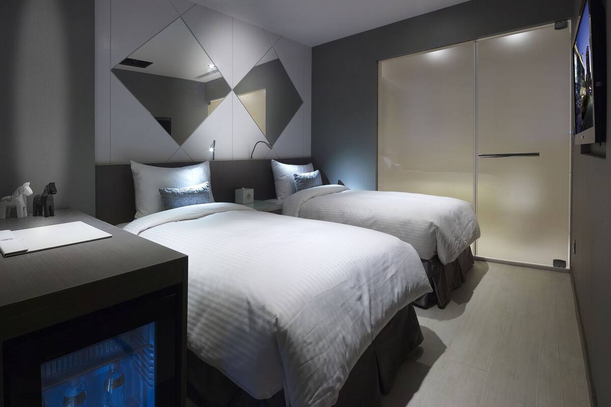 Moderni hotellihuone, jossa on kaksi sänkyä, työpöytä ja vaatekaappi.