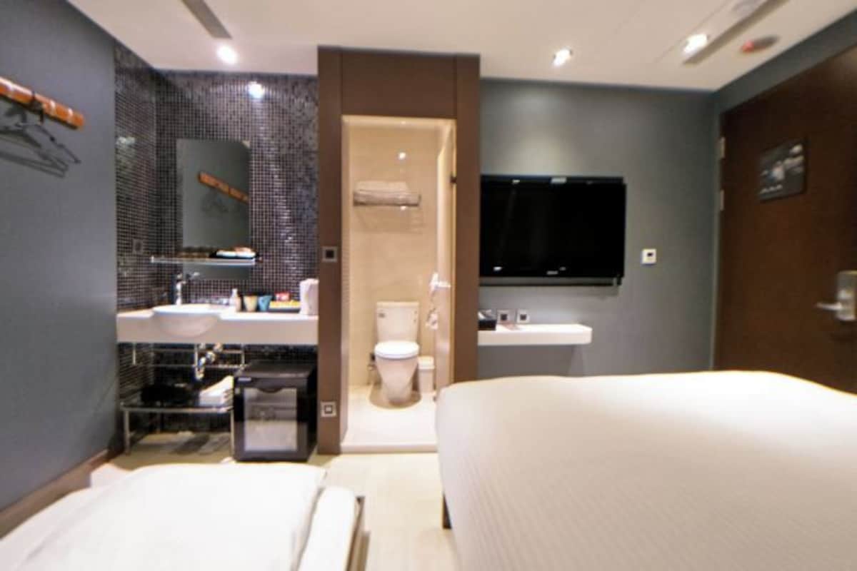 Une chambre d’hôtel moderne dotée d’un grand lit, d’une salle de bain séparée avec des toilettes et un lavabo, et d’un téléviseur à écran plat fixé au mur.