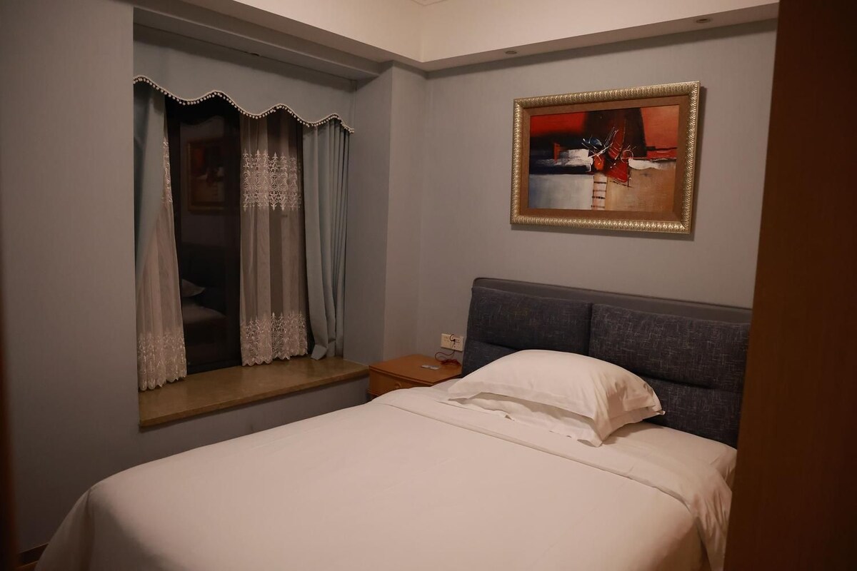 Une chambre d’hôtel avec un lit, une table de chevet, une fenêtre avec des rideaux et un tableau au mur.