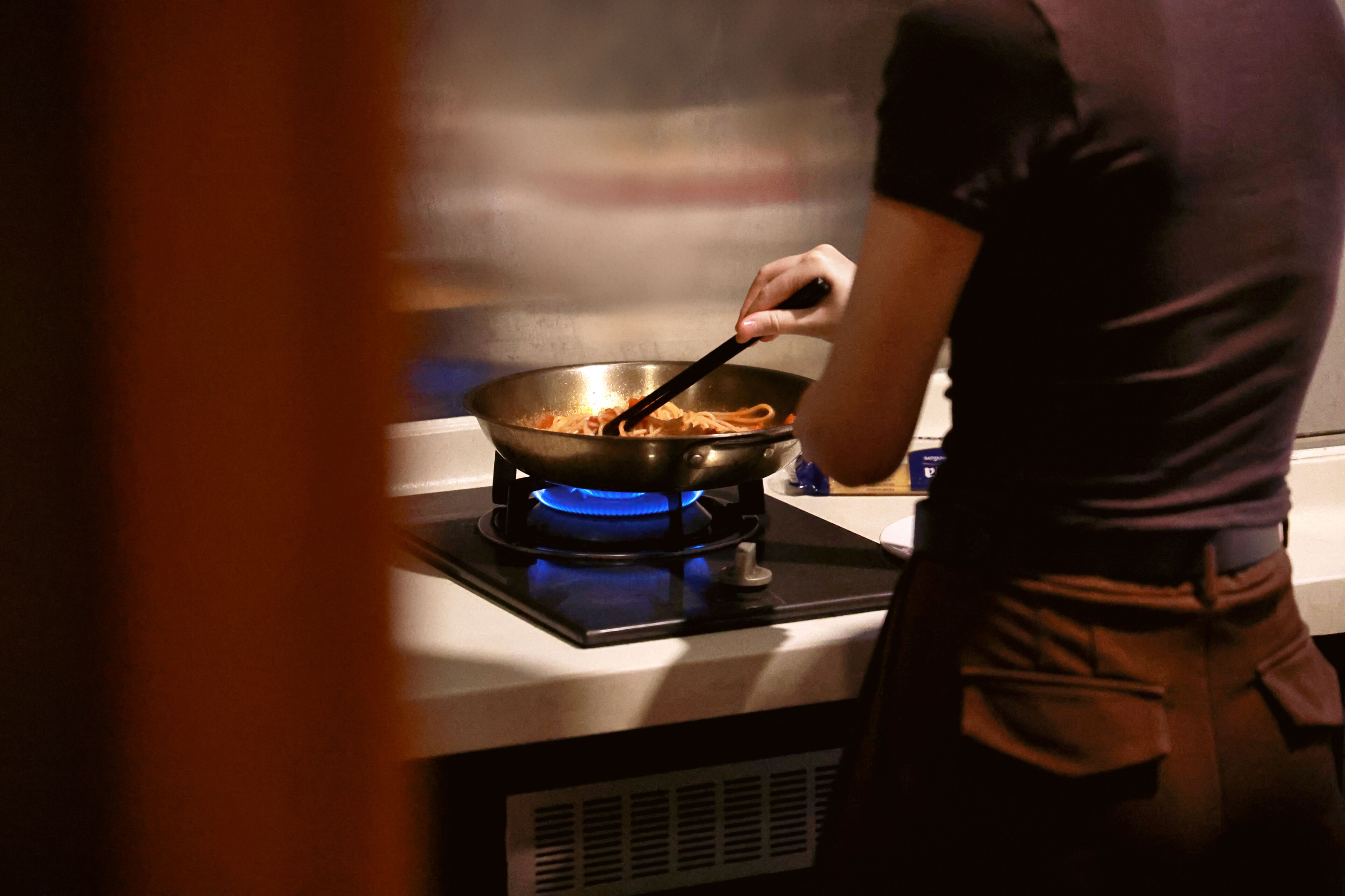 A person cooking on a stove with a pan.