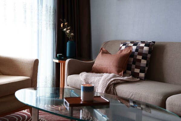 A modern living room with a glass coffee table, a beige sofa with patterned cushions, a blue vase with flowers, and a striped rug. - Dan Executive Apartment Guangzhou (Guangzhou)