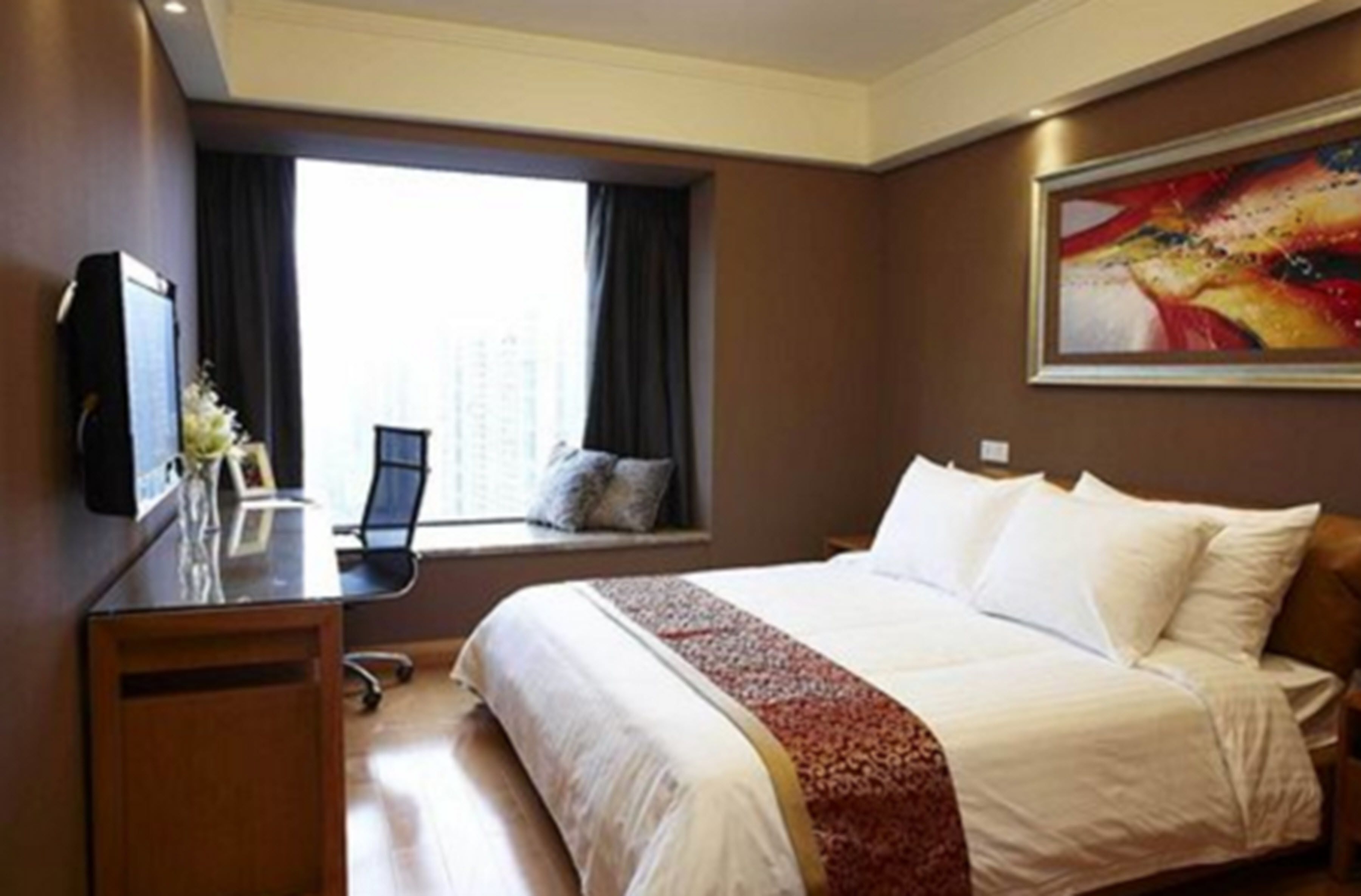 A hotel room with a bed, a desk, a chair, a TV, and a window with a view of buildings.