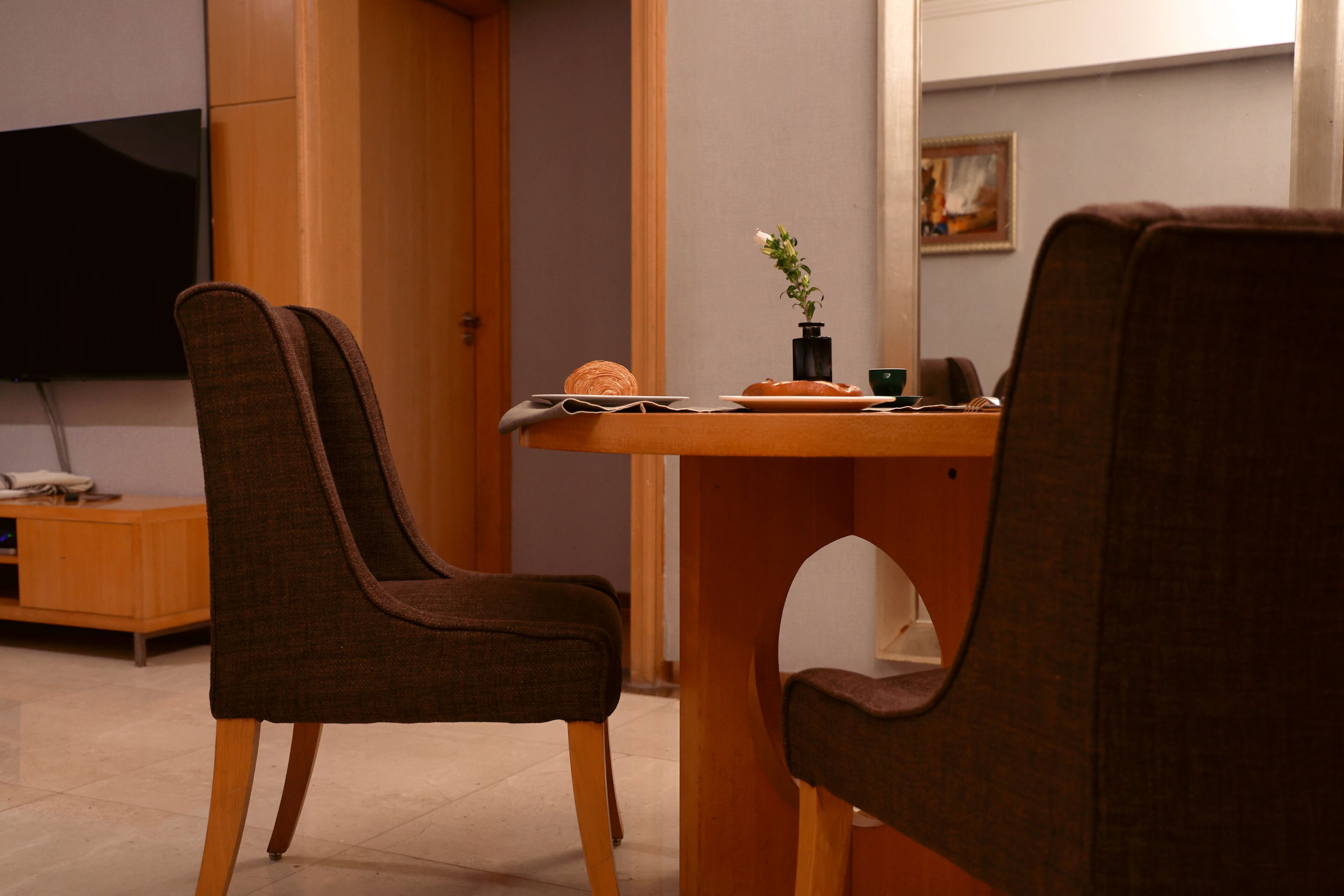 A room with a dining table, two chairs, a television, a cabinet, and a small plant.