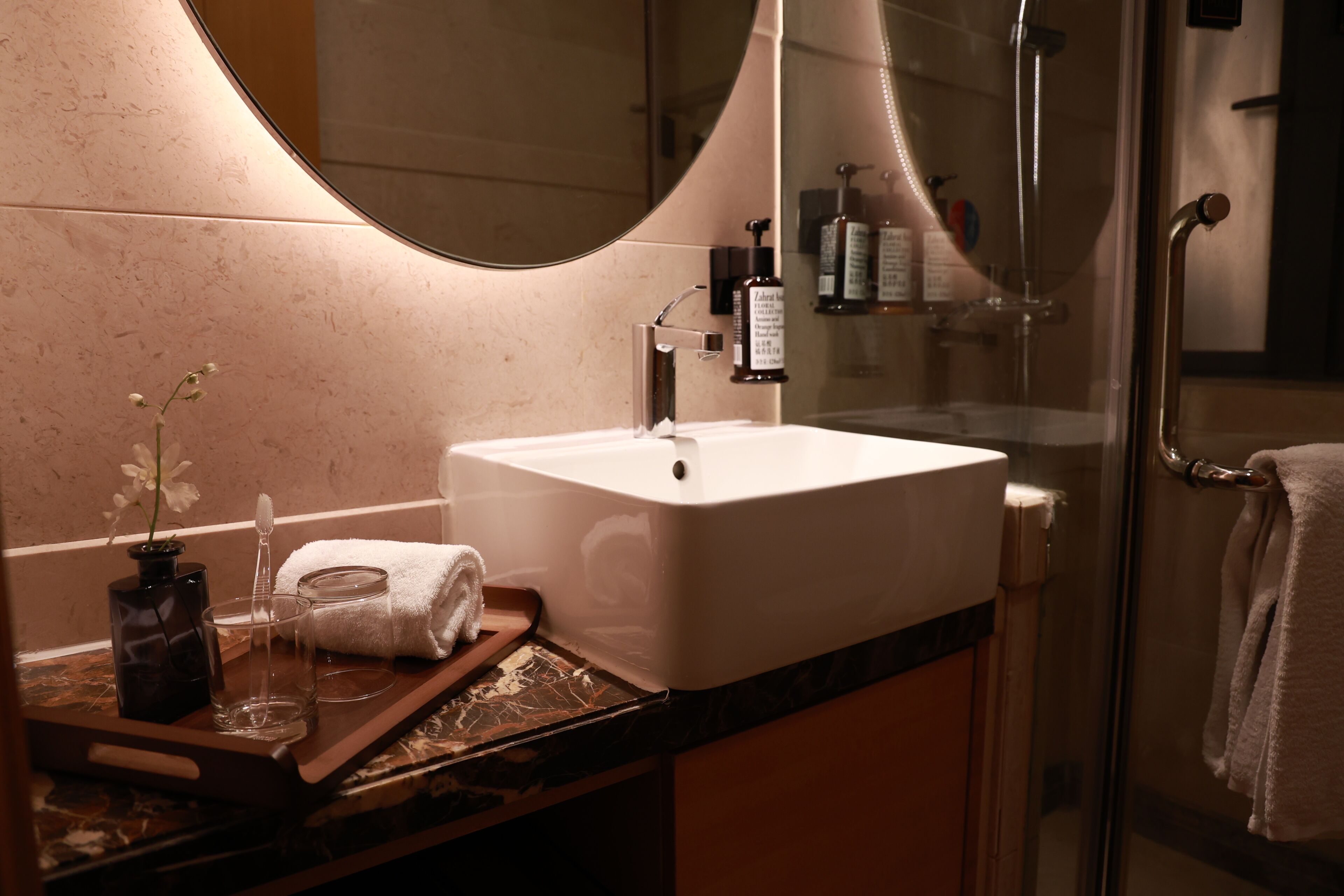 A bathroom with a large mirror, a white sink, a glass shower enclosure, and a towel rack.