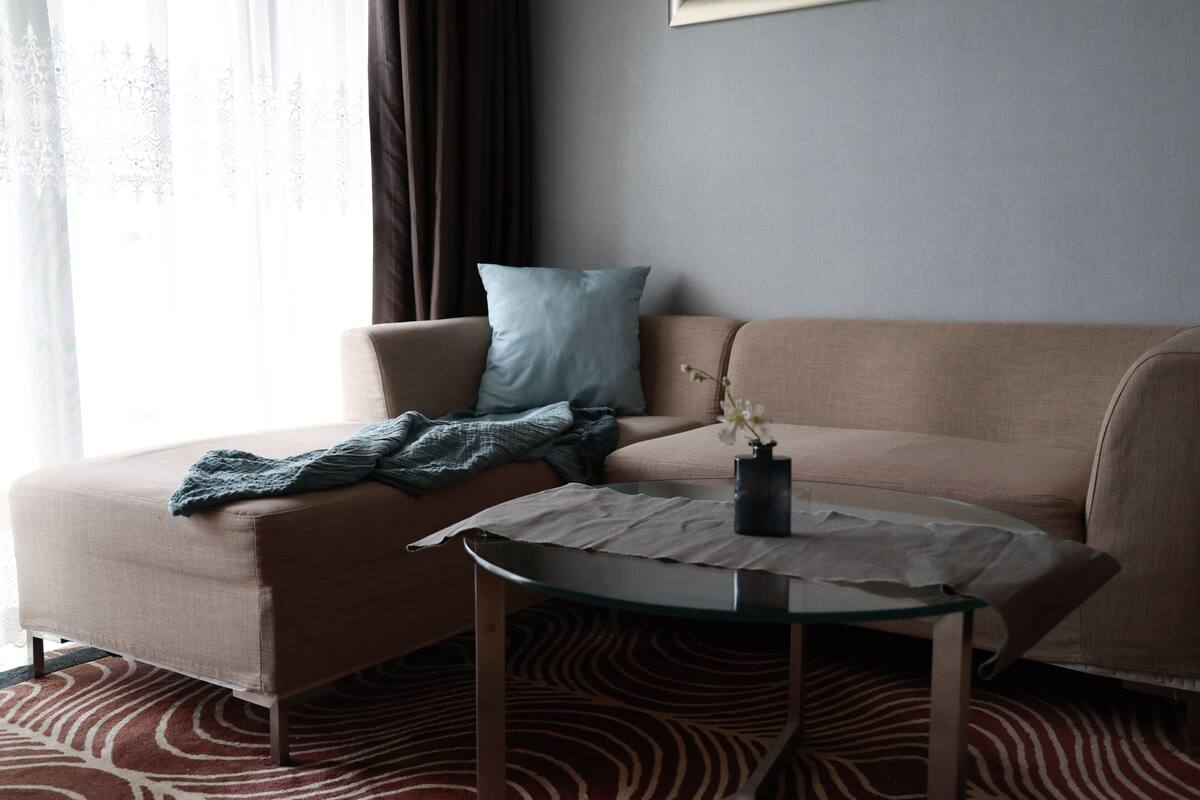 A modern living room with a beige sofa, a glass coffee table, and a patterned rug.