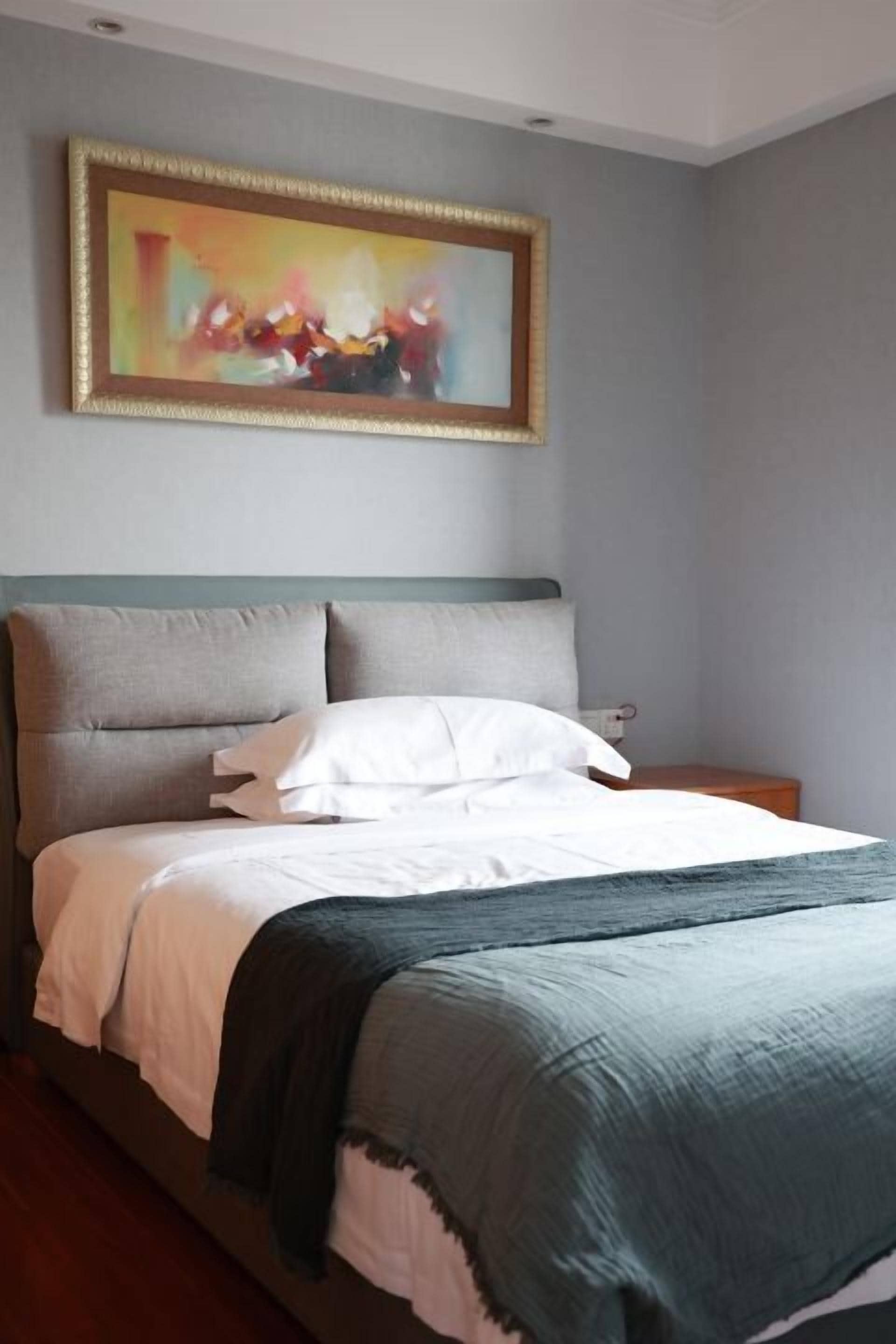 A bedroom with a bed, a nightstand, a painting, and a gray headboard.