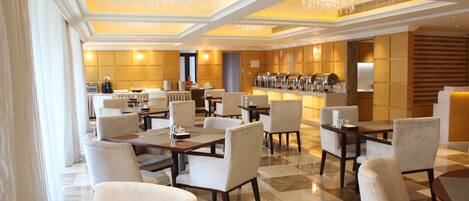 Un amplio hall de hotel con varias zonas de estar, un bar y vistas al área de la cocina.