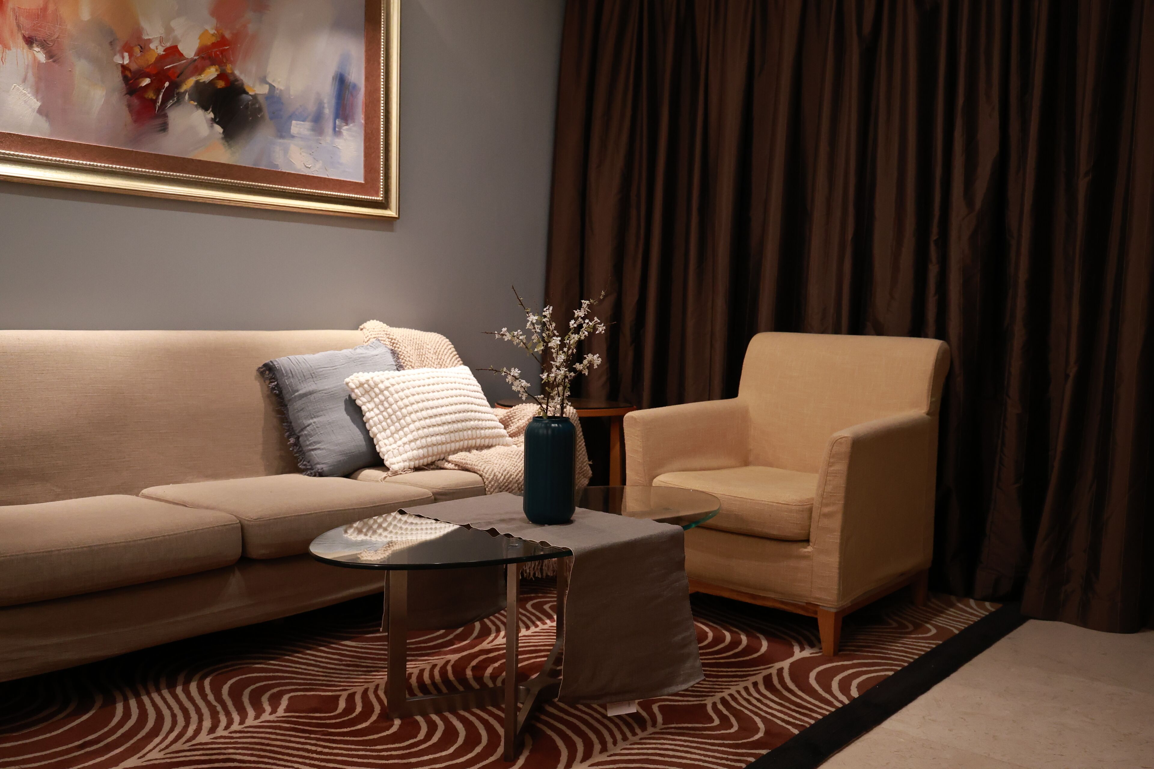 A living room with a sofa, armchair, coffee table, and a painting on the wall.
