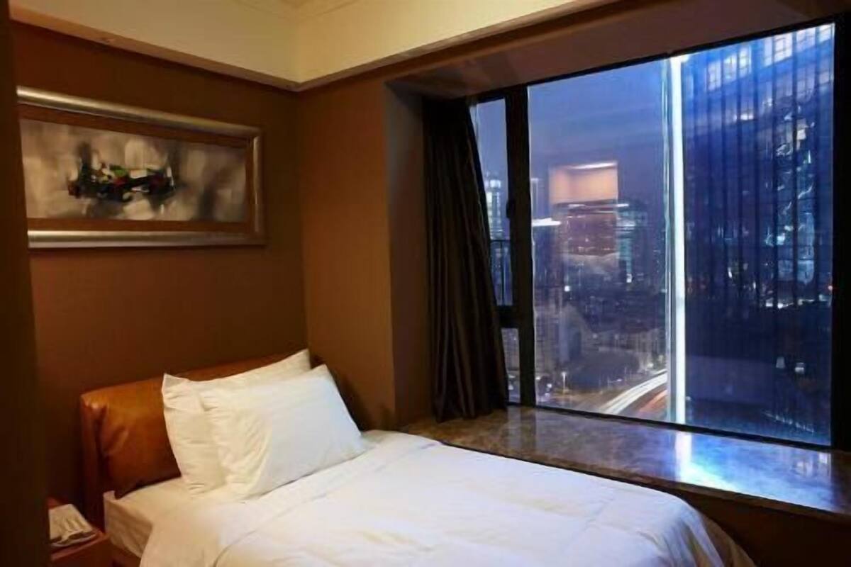 A hotel room with a large window, a bed, and a painting on the wall.