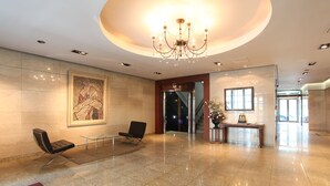 A spacious lobby with a chandelier, a large abstract painting, a reception desk, and a staircase leading to the upper floors. - Karak Tourist Hotel (Seoul)