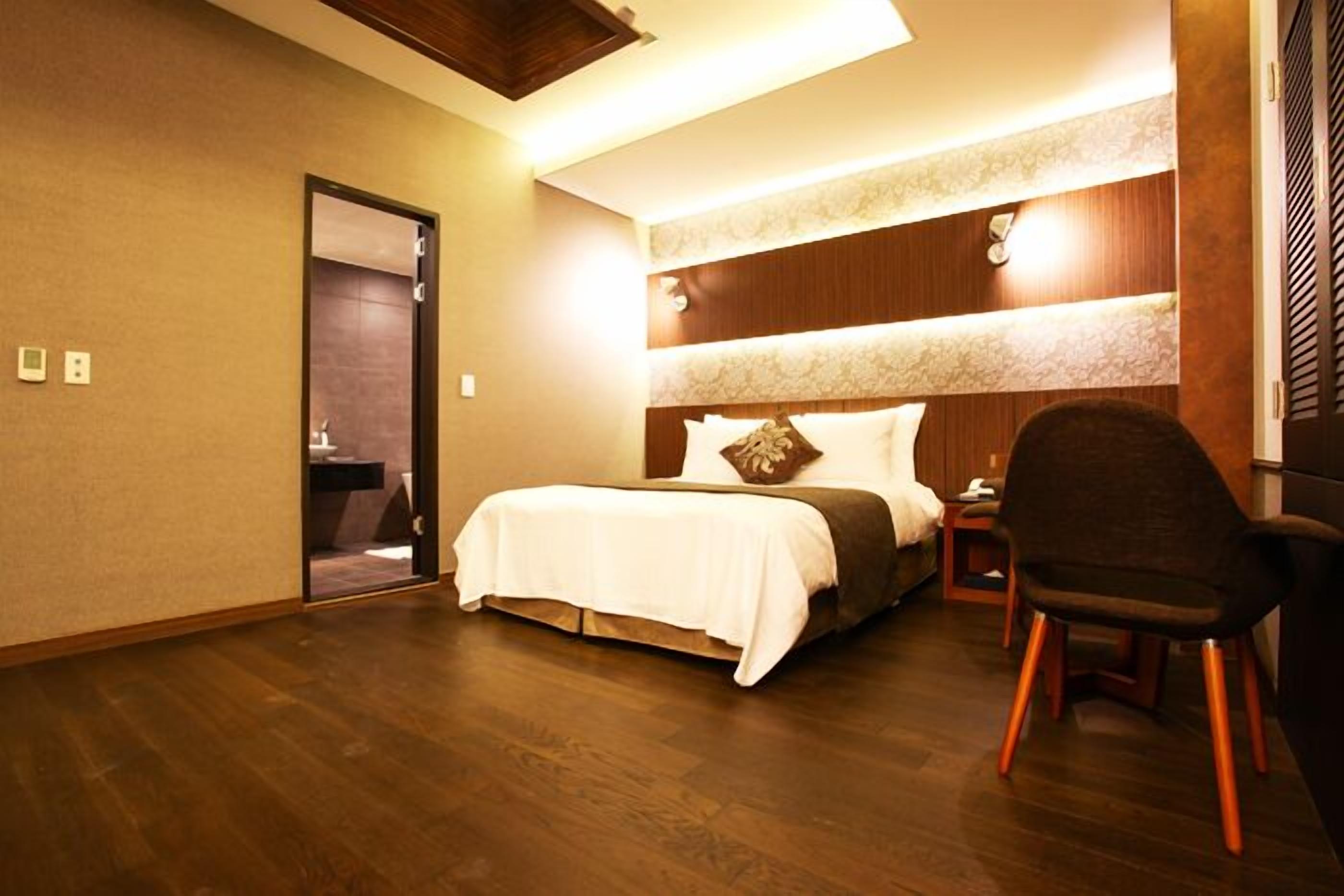 A hotel room with a large bed, a chair, a nightstand, and a mirror.