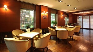 A restaurant with wooden flooring, beige chairs, and tables. There are windows with views of greenery. - Karak Tourist Hotel (Seoul)