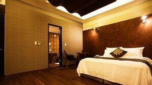 A hotel room with a wooden floor, a bed with white bedding, a nightstand, a chair, and a door leading to a bathroom. - Karak Tourist Hotel (Seoul)